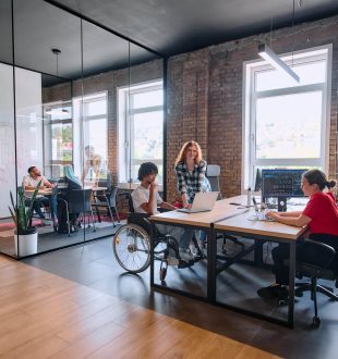 A diverse group of business professionals collaborates in a modern startup coworking center, utilizing a mix of paper-based and technological tools such as mobile phones and computers .