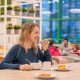 beautiful girl with long blonde hair in a bright sweater is emotionally happy to talk on the speakerphone on the phone in a cafe. break. Lunch;Breakfast