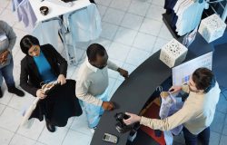 Cashier at clothing store checkout desk scanning and processing purchase for customer top view. Diverse people standing in line at counter desk while boutique employee using scanner