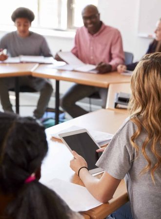 Female High School Student Using Digital Tablet Whilst Sitting At Desk In Class