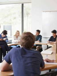 Female High School Tutor Sitting At Table With Pupils Teaching Maths Class