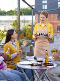 A group of friends enjoying sushi and drinks at an outdoor restaurant, served by a friendly waitress.