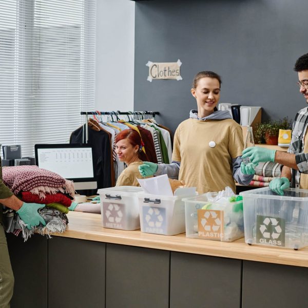 Group of volunteers sorting trash in garbage bins and preparing second hand clothes for people in need while working in office