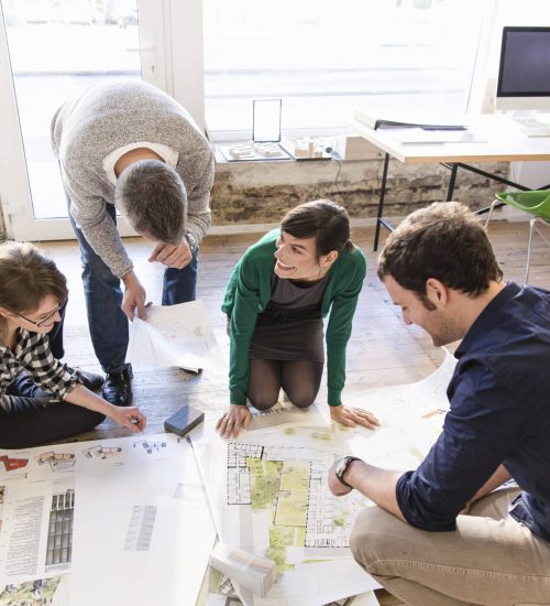 High angle view of architects on office floor discussing blueprint